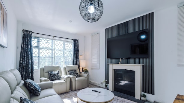 A living room with a sofa, armchairs, a fireplace, a TV, and a patterned rug. - Luxury 3 Bed - 6 min to Airport  (Cheadle)