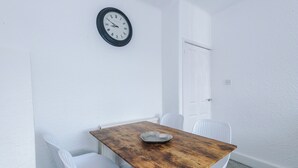 A room with a wooden table, white chairs, a wall clock, and a white door. - Luxury 3 Bed - 6 min to Airport  (Cheadle)