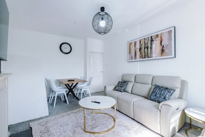 A living room with a sofa, a round coffee table, a dining table with chairs, a clock, and a painting on the wall. - Luxury 3 Bed - 6 min to Airport  (Cheadle)