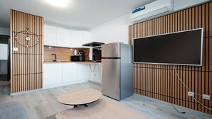 Et moderne køkken med indbygget mikroovn, komfur og køleskab, et stort fladskærms-tv monteret på væggen, samt et lille rundt bord.