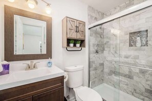 Une salle de bain avec une douche à parois de verre, un meuble en bois agrémenté de plantes, des toilettes blanches et un grand miroir.