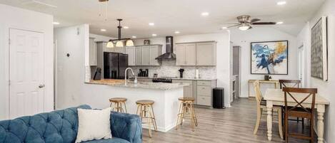 A modern kitchen with a central island, bar stools, and a dining area with wooden chairs.