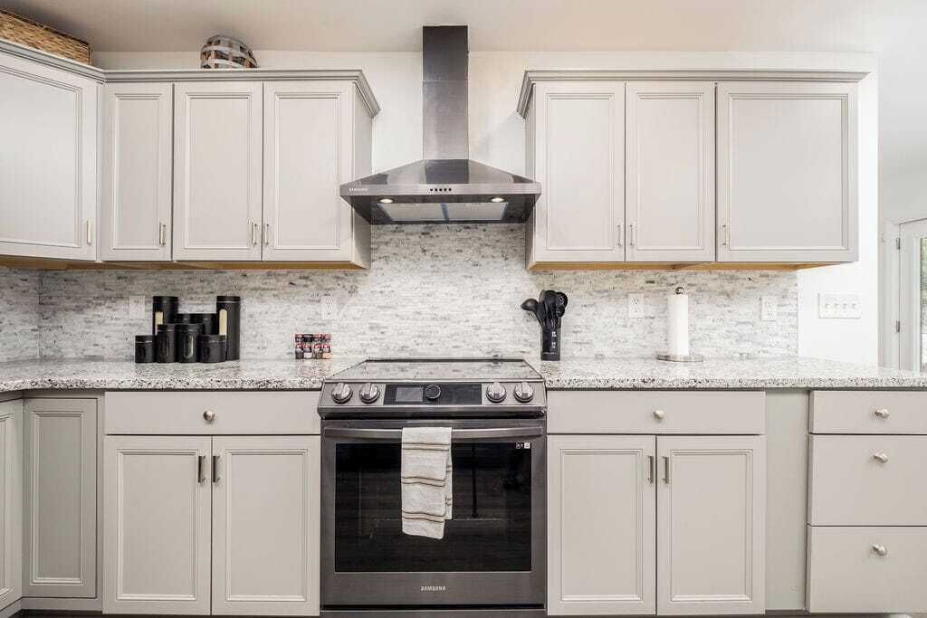 Cocina con alacenas blancas, extractor de acero inoxidable, horno Samsung y encimeras de granito.