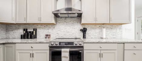 Cocina con alacenas blancas, extractor de acero inoxidable, horno Samsung y encimeras de granito.