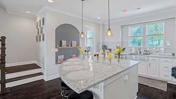 A kitchen with a granite island, bar stools, pendant lighting, and a view of the outdoors through large windows.