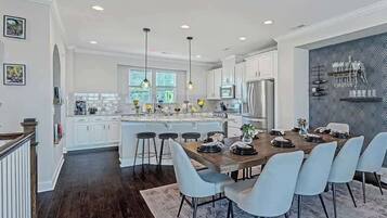 A modern kitchen with white cabinets, a central island, bar stools, and a dining table with chairs.