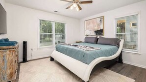 Une chambre à coucher avec un lit à la forme arrondie, un ventilateur de plafond et deux fenêtres équipées de stores.