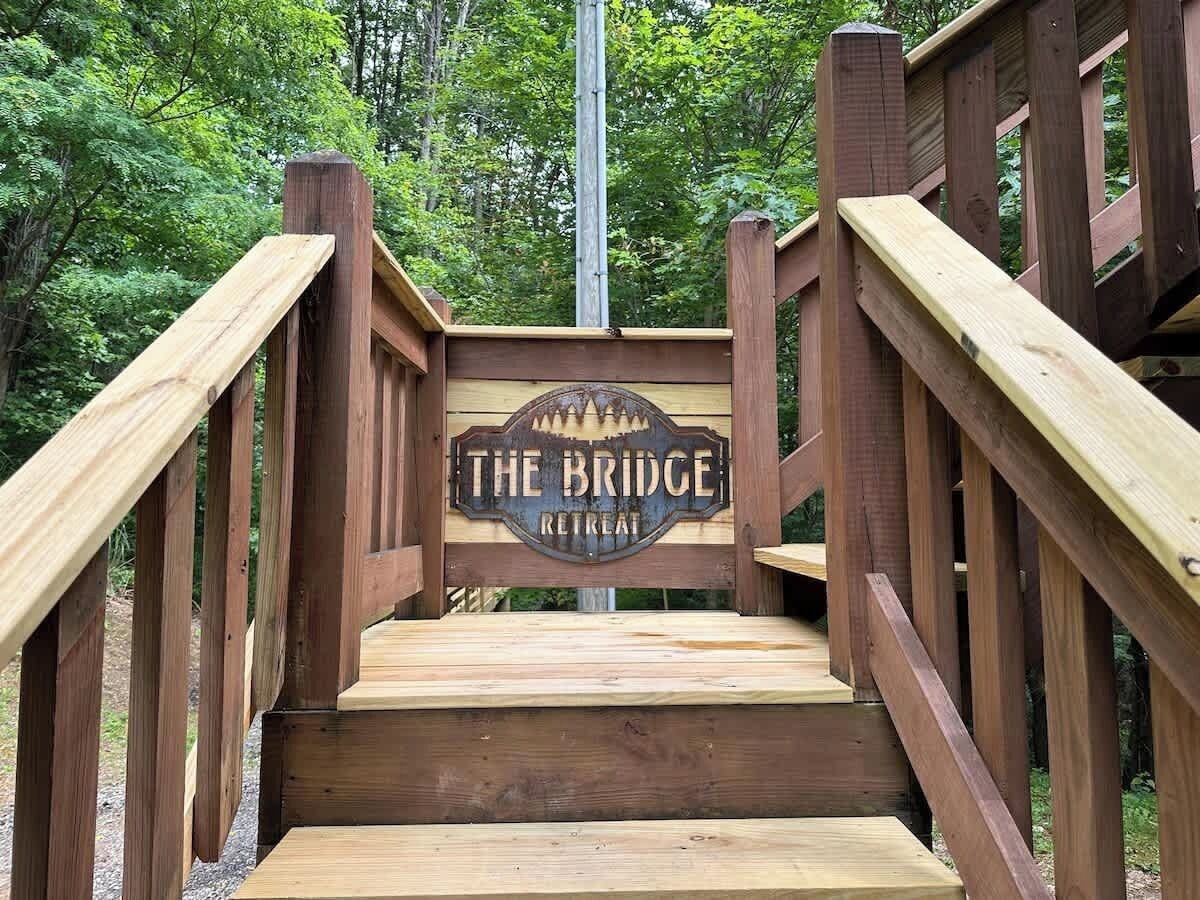 Eine hölzerne Treppe führt zu einem Schild mit der Aufschrift 'The Bridge Retreat'.