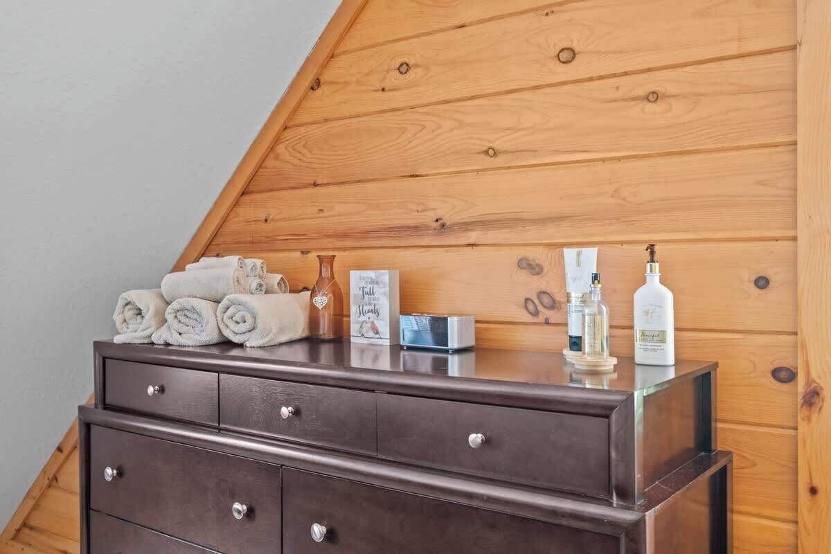 Techo de madera con diseño inclinado, un aparador de madera oscura con cajones y artículos de tocador encima.