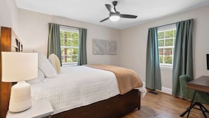 A bedroom with a bed, a desk, a chair, a ceiling fan, and a window with curtains. - West End Hideaway - Enderly Park - Fruit Trees (Charlotte)