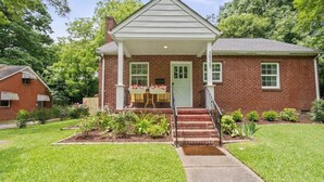 A two-story brick house with a front porch, a small garden, and a visible mailbox. - West End Hideaway - Enderly Park - Fruit Trees (Charlotte)