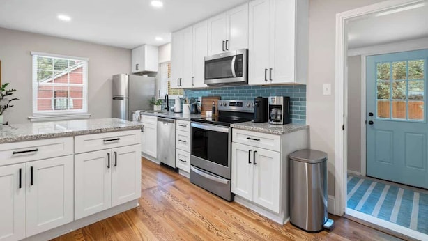 A modern kitchen with white cabinets, stainless steel appliances, and a blue door. - West End Hideaway - Enderly Park - Fruit Trees (Charlotte)