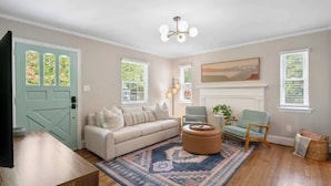 A living room with a sofa, armchair, ottoman, and a fireplace. - West End Hideaway - Enderly Park - Fruit Trees (Charlotte)
