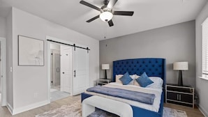 Una camera da letto con un letto, un ventilatore a soffitto, un comodino e una porta.