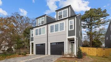 A modern two-story house with a garage, a fenced yard, and a clear sky.