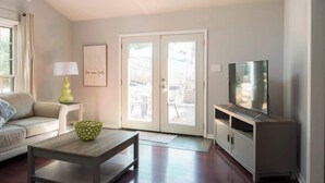 A living room with a sofa, coffee table, TV stand, and a door leading to an outdoor area.