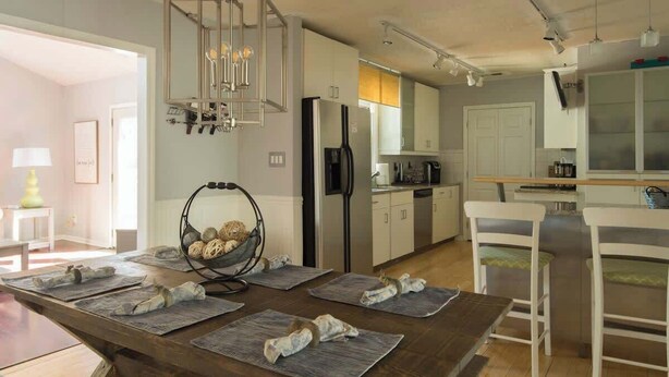A modern kitchen with white cabinets, a black refrigerator, and a dining area with a wooden table and white chairs.