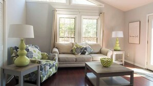 A living room with a sofa, two side tables, a coffee table, and a window with curtains.