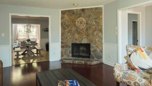 A living room with a stone fireplace, a dining table with benches, and a patterned sofa.