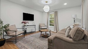 A modern living room with a sofa, chairs, a TV, a plant, and a window with curtains. - Family/Pet Friendly - Professional Design (Concord)