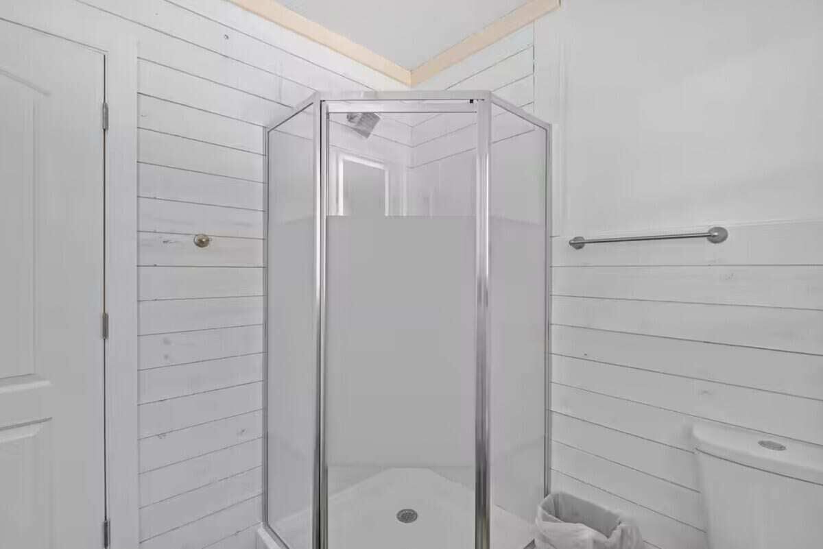 A bathroom with a glass-enclosed shower, white wooden walls, a white toilet, and a white sink.