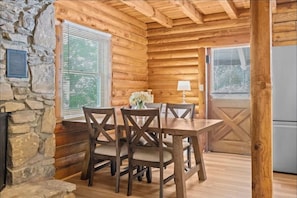 Un intérieur en bois avec un mur en pierre, une table à manger avec des chaises et une fenêtre avec des stores.