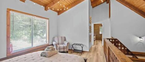 A bedroom with a large bed, a chair, a wooden staircase, and a window with blinds.