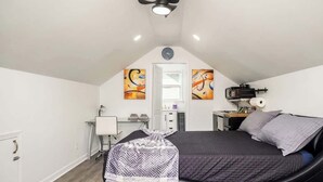 Ein Schlafzimmer mit einem Bett, einem Schreibtisch, einem Sessel, einem Deckenventilator und Bildern an den Wänden.