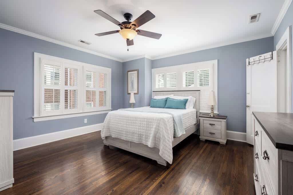 Une chambre à coucher comprenant un lit, des tables de chevet, une commode, un ventilateur de plafond et des fenêtres équipées de volets.