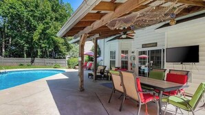 A covered outdoor area with a pool, patio furniture, and a television. - Pool is Open! 4BR Retreat • Gameroom • Sleeps 12 (Charlotte)