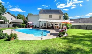 Un patio trasero con piscina, un porche cubierto y una casa.
