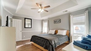 A bedroom with a bed, a ceiling fan, a window with curtains, a bedside table, and a stack of towels. - Pool is Open! 4BR Retreat • Gameroom • Sleeps 12 (Charlotte)