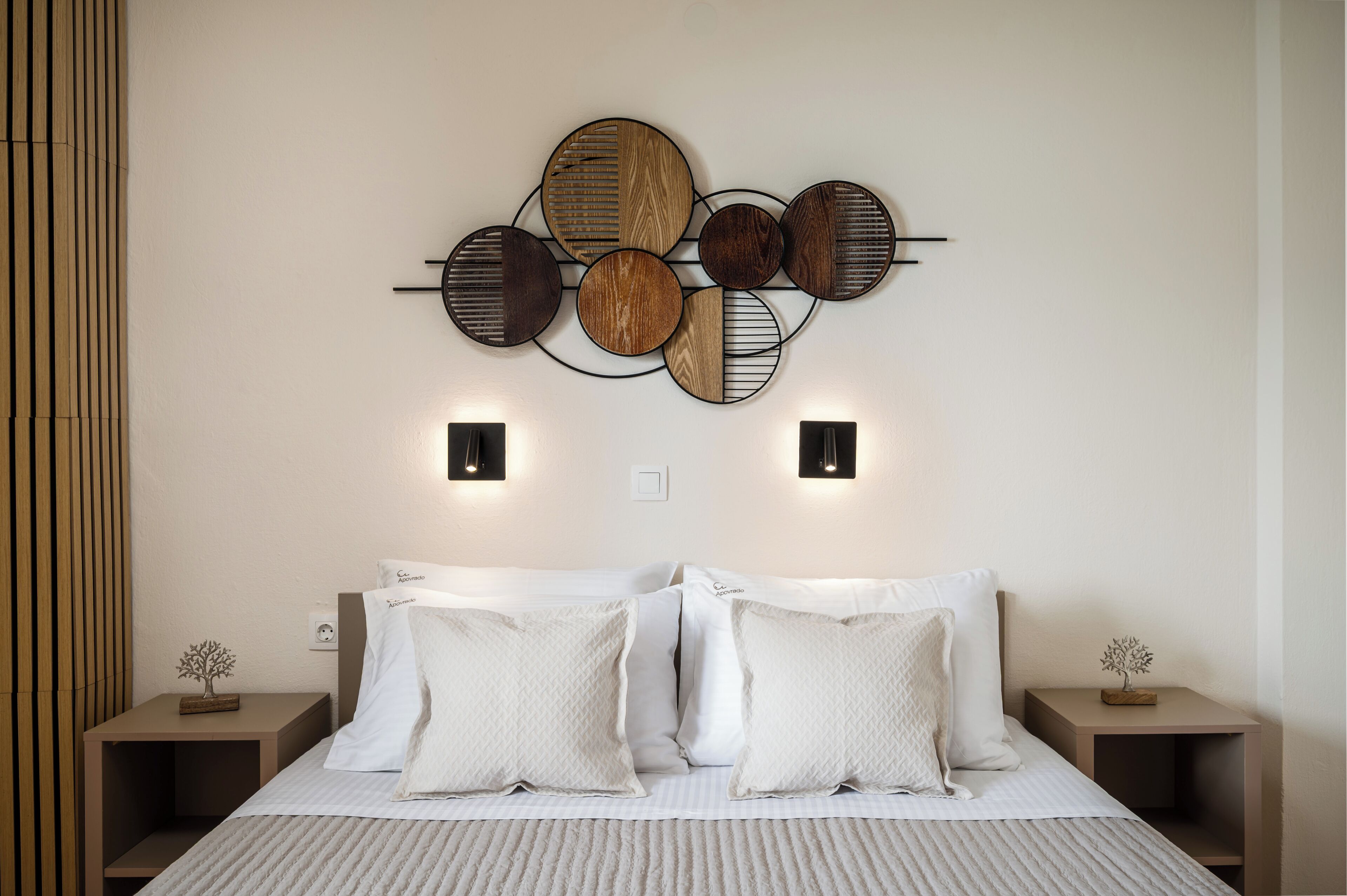 Un dormitori amb un llit, dues taules de nit, una làmpada de paret i una obra d'art de fusta decorativa.
