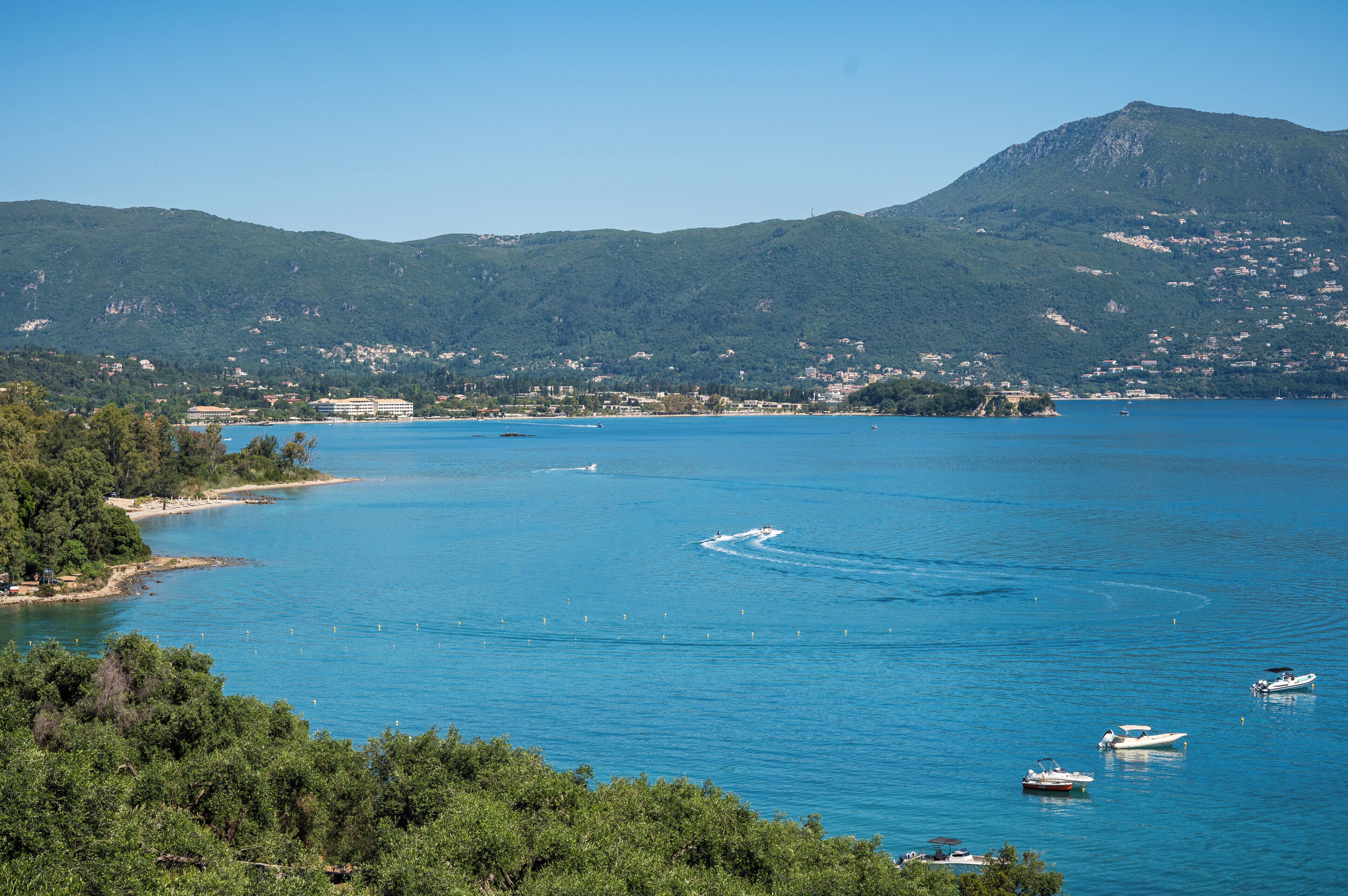 Eine Küstenlandschaft mit einem Berg, klarem, blauem Wasser und Booten.