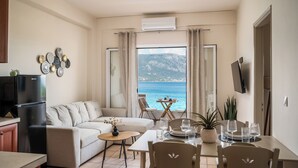 A modern living room with a sofa, dining table, chairs, a TV, and a view of the sea. - Apovrado Stay by Konnect, Kommeno (Corfu)