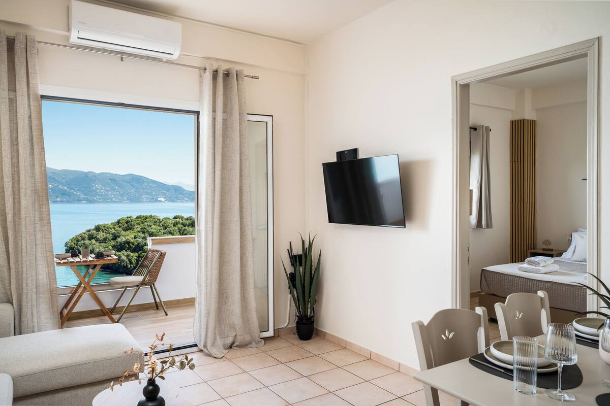 A hotel room with a balcony, a TV, a dining area, and a bed.
