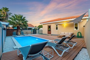 Ein Swimmingpool mit Liegestühlen, einer Palme und einem Haus mit Ziegeldach.