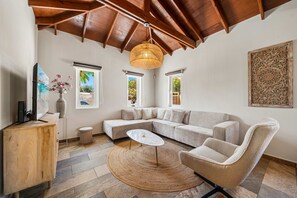 Ein modernes Wohnzimmer mit einer Eckcouch, einem runden Couchtisch, einer Hängeleuchte aus Rattan und einer Wanddekoration.