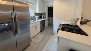 A modern kitchen with stainless steel appliances, white cabinetry, and a gas stove. - Captivating Rose Cottage-3 King Beds-College Hill (Wichita)
