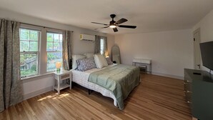 A bedroom with a bed, a nightstand, a dresser, a ceiling fan, and a window with curtains. - Captivating Rose Cottage-3 King Beds-College Hill (Wichita)