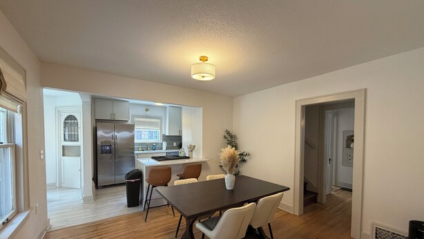 A modern kitchen with stainless steel appliances, a dining area with a dark wooden table and white chairs, and a hallway leading to other rooms. - Captivating Rose Cottage-3 King Beds-College Hill (Wichita)