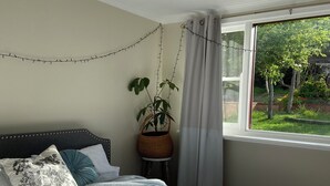 A bedroom with a bed, a potted plant, and a window with a view of greenery.