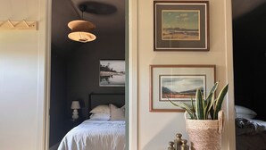 A bedroom with a bed, a bedside table with a plant, and two framed pictures on the wall. - Home away from home in quiet village near Lake Erie. (Selkirk)