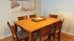 Ein Essbereich mit Holztisch und -stühlen, einer Pendelleuchte und einem Gemälde mit Strandmotiv an der Wand.