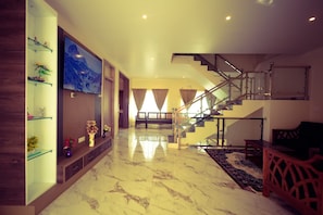 A spacious living area with a marble floor, a staircase, and a TV mounted on the wall.