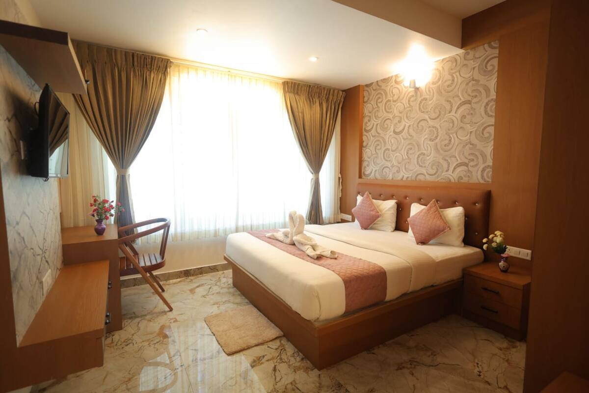 Une chambre d’hôtel comprenant un lit, un bureau, une chaise, une télévision et une table de chevet ornée d’un vase de fleurs.