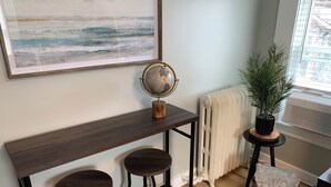 A room with a wooden bench, two stools, a globe, a radiator, a potted plant, and a large abstract painting. - Cozy 1-bedroom apartment with parking in walkable Portland location (Portland)