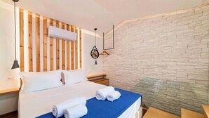 Ein Hotelzimmer mit Bett, Wand-Klimaanlage, Holz-Kopfstück und blauer Bettdecke, sowie einer Wand mit Steinoptik.