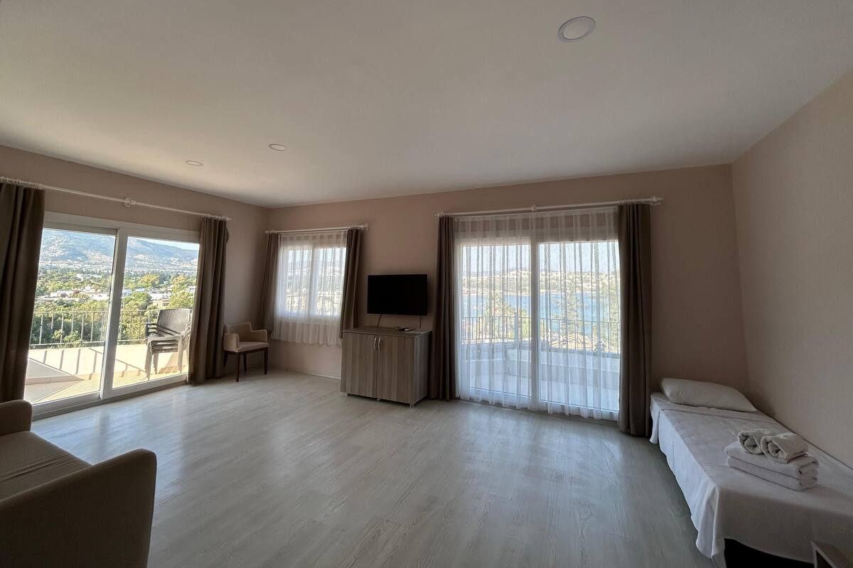 Habitación de hotel con balcón, televisor, cama y zona de estar.