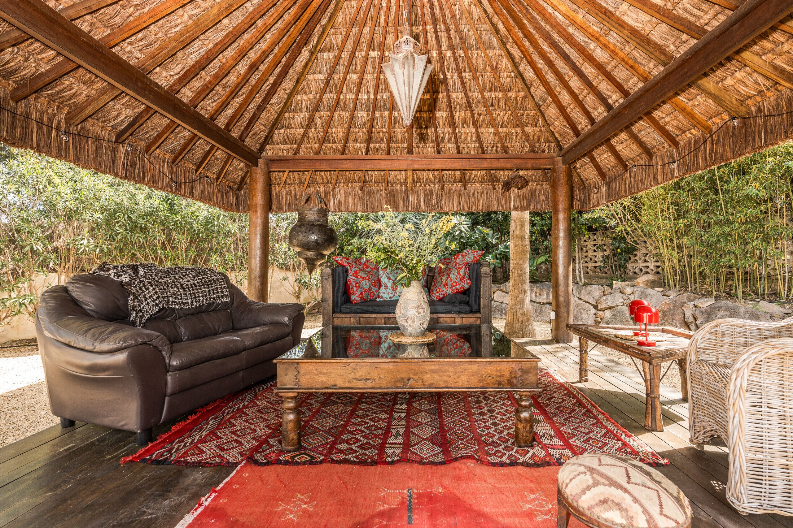 A covered outdoor seating area with a thatched roof, a sofa, a coffee table, and a wicker chair.